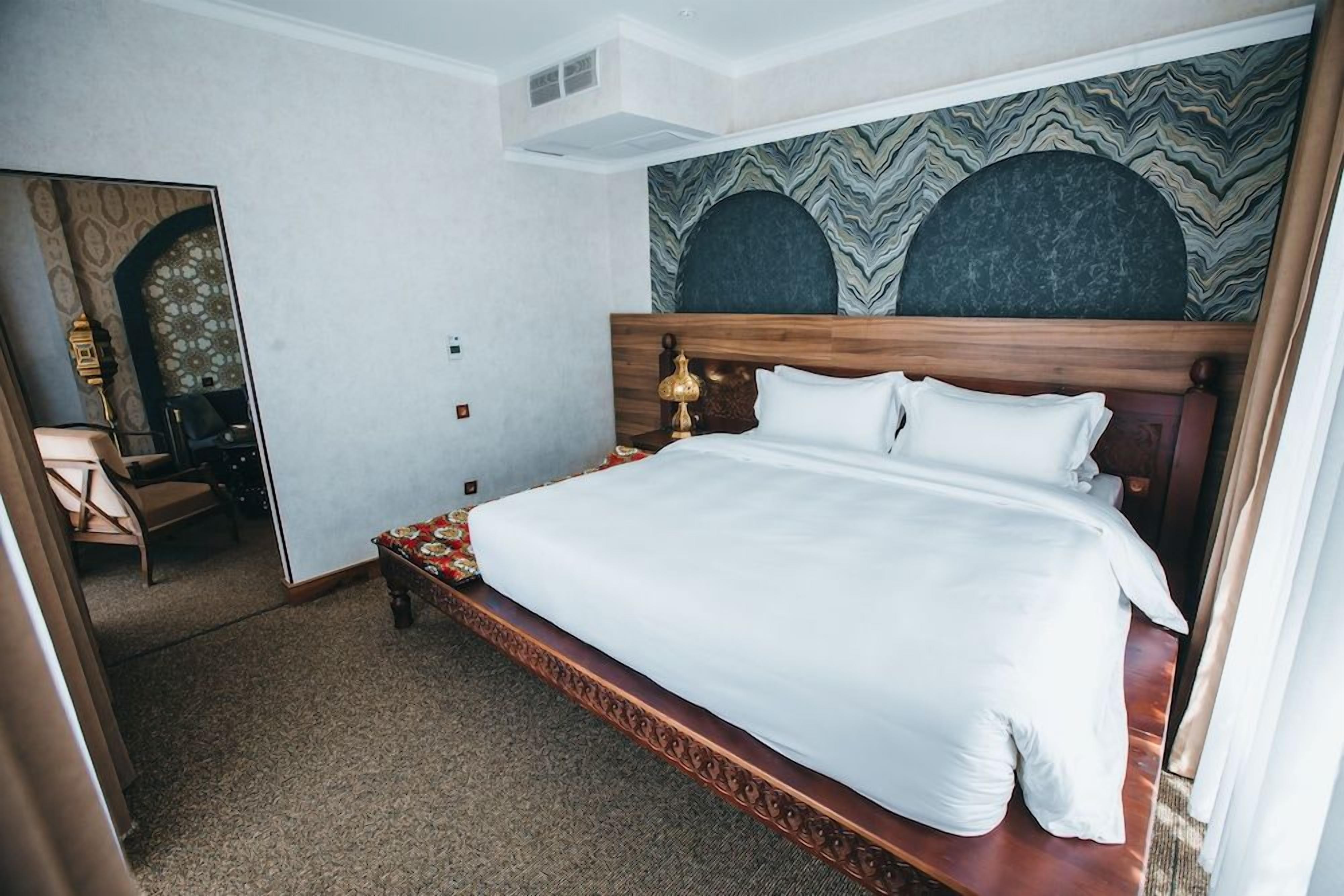Quarto de hotel com uma cama grande, cabeceira de madeira e parede estampada.