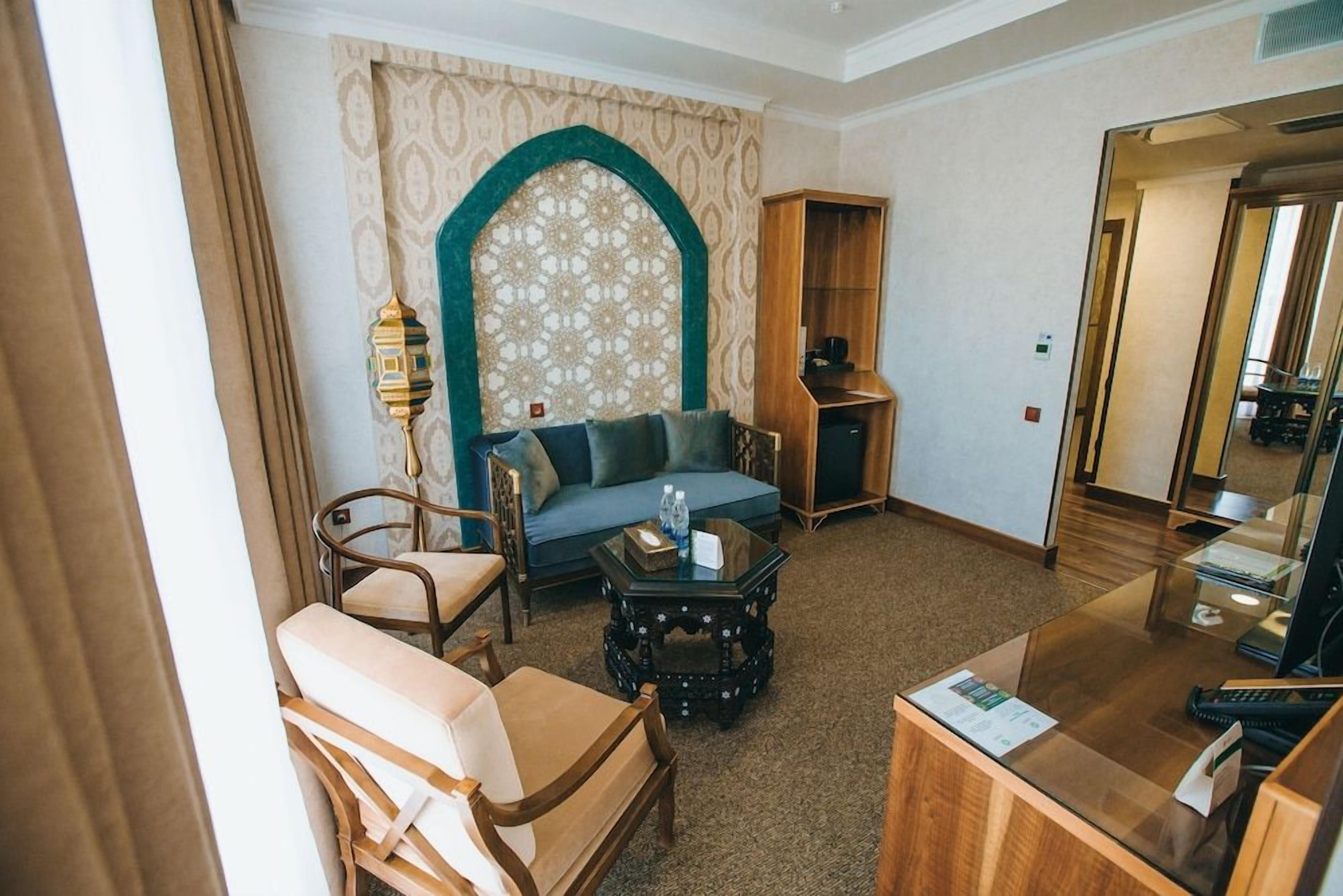 A hotel room with a sofa, armchairs, a coffee table, a desk, and a bookshelf.