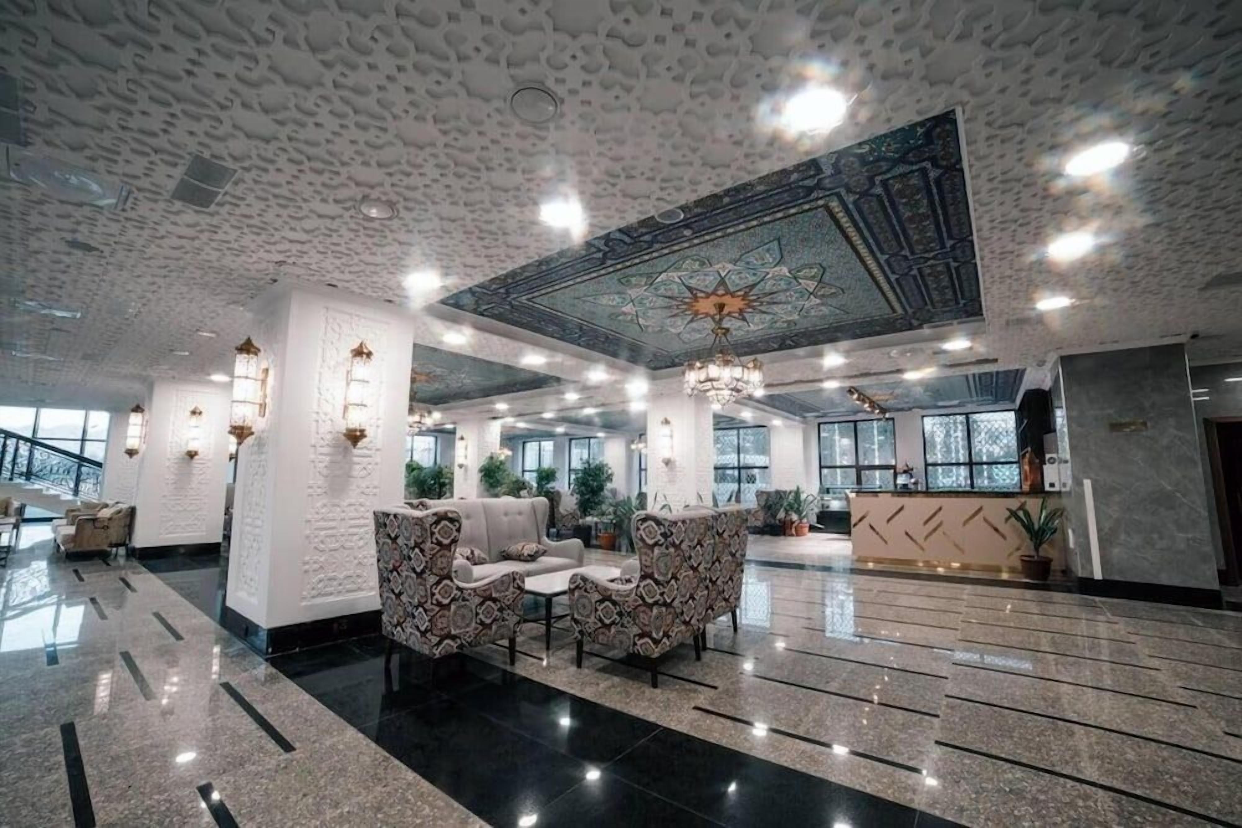 A spacious lobby with patterned sofas, a chandelier, and a decorative ceiling.
