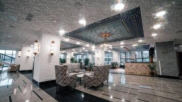 A spacious lobby with patterned sofas, a chandelier, and a decorative ceiling.