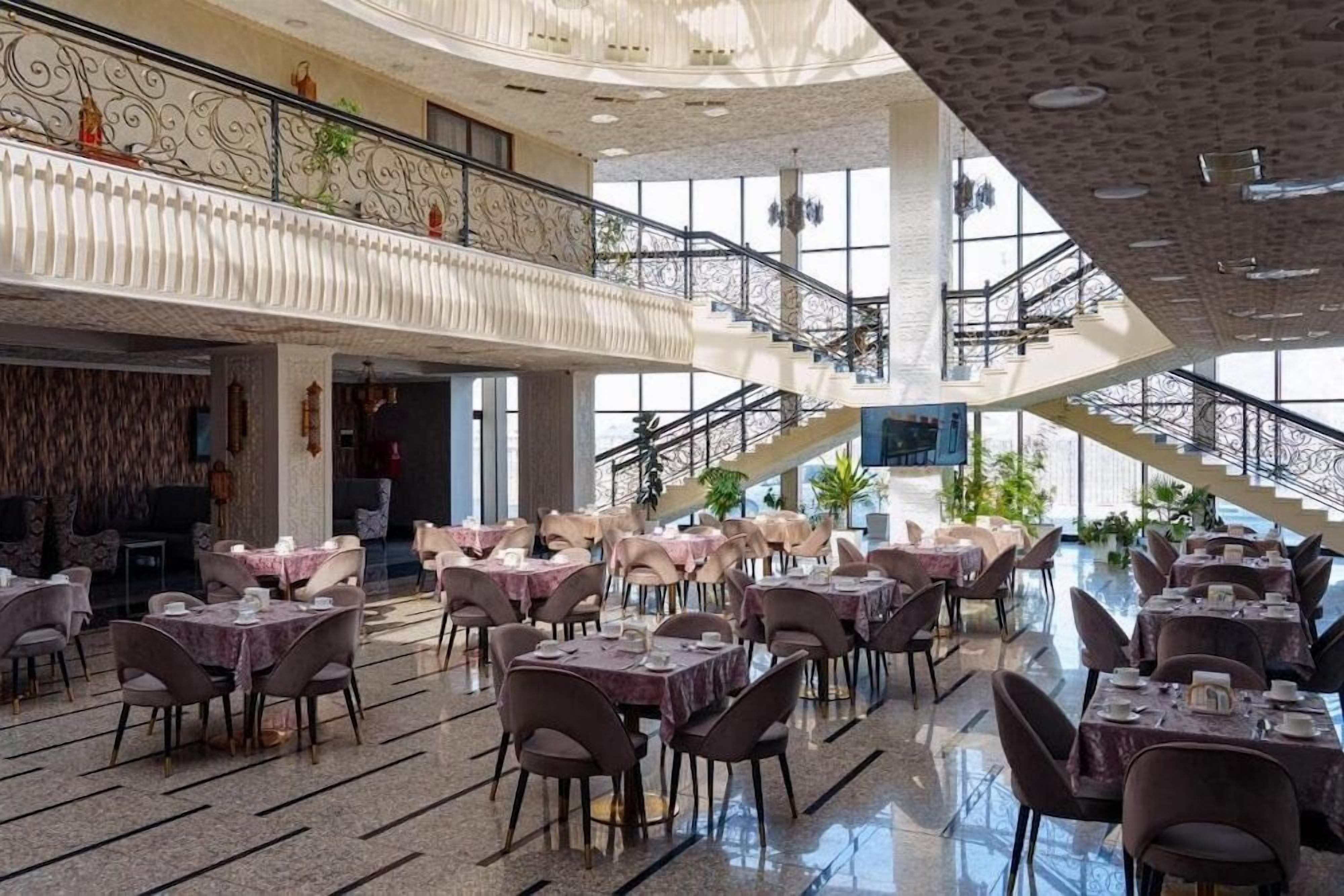 Un vaste espace intérieur aménagé en salle à manger, avec de nombreuses tables et chaises, un balcon doté de balustrades décoratives et un escalier reliant les différents niveaux.