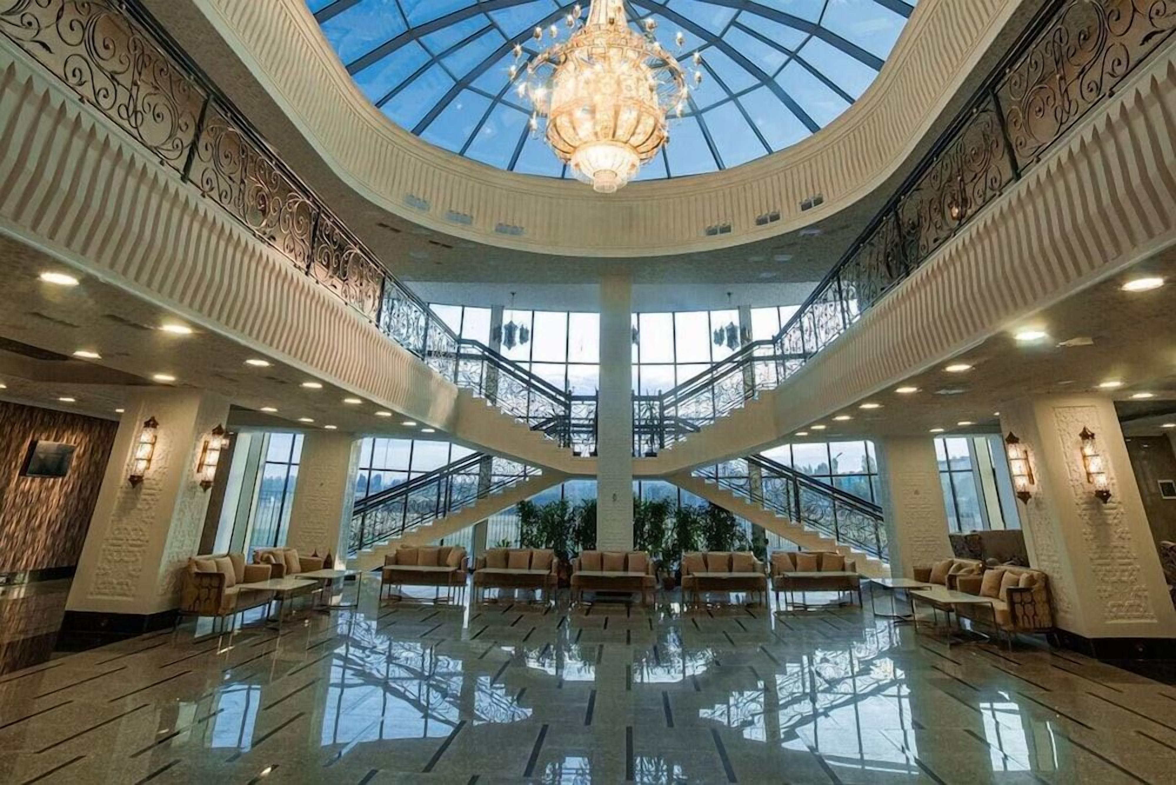 En rymlig entréhall med en central trappa, en kristallkrona och sittgrupper.