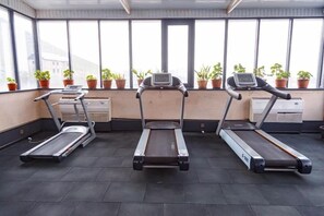 A gym with three treadmills aligned in a row, large windows with potted plants, and a visible air conditioning unit. - Jannat Resort Osh (Osh)