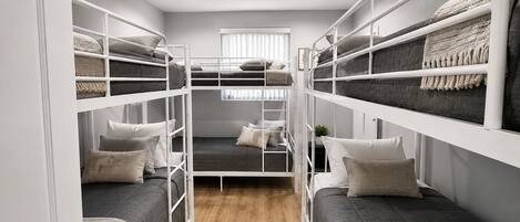 A bunk bed room with a wooden floor, white railings, and a window with blinds.