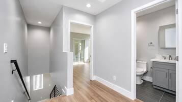 A modern interior with a staircase, a hallway leading to a bathroom, and a view of a balcony.