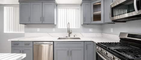 Una cocina moderna con armarios grises, un lavavajillas de acero inoxidable, una estufa a gas y un horno empotrado.