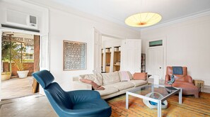 Een woonkamer met een bank, een blauwe stoel, een glazen salontafel en een decoratieve lamp.