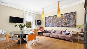 Een moderne woonkamer met een eethoek, een bank, een televisie en een groot abstract schilderij.