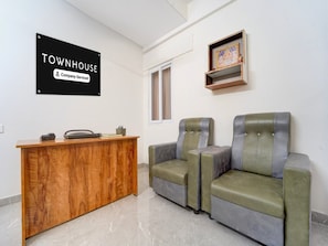 A reception area with a wooden desk, two cushioned chairs, a sign reading 'TOWNHOUSE Company Serviced', and a shelf with framed artwork.