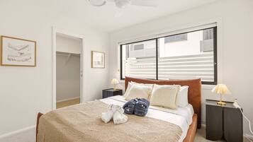 A bedroom with a bed, a ceiling fan, a window with blinds, a nightstand with a lamp, and a door leading to a closet.