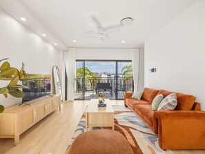 A modern living room with a sofa, coffee table, and TV on a wooden cabinet. - BrandNew|DuctedAC|Walk to Train&Shop|Double Garage (Oxley)