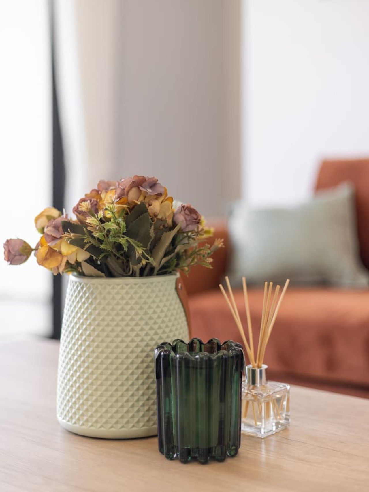 Et bord med en vase i taktil tekstur, tørrede blomster, en grøn glasflaske og et klart glas med rør.