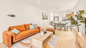 A modern living room with a sofa, coffee table, and dining area. - BrandNew|DuctedAC|Walk to Train&Shop|Double Garage (Oxley)