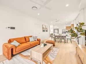 A modern living room with a sofa, coffee table, and dining area. - BrandNew|DuctedAC|Walk to Train&Shop|Double Garage (Oxley)