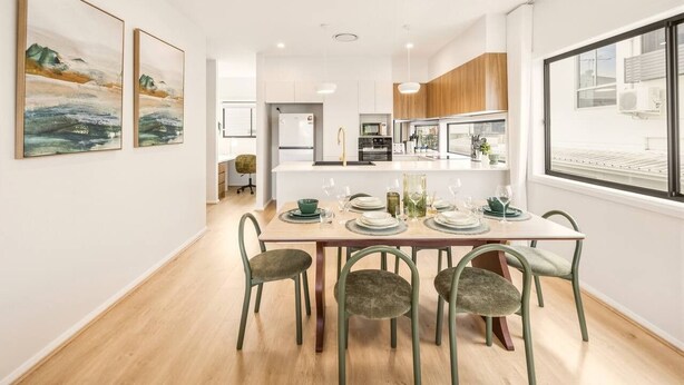 A modern kitchen with white cabinets, a central island, and a dining area with a table set for four. - BrandNew|DuctedAC|Walk to Train&Shop|Double Garage (Oxley)