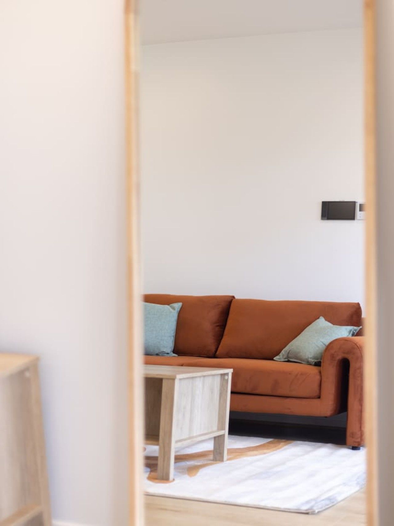 A room with a brown sofa, a small wooden side table, and a white rug.