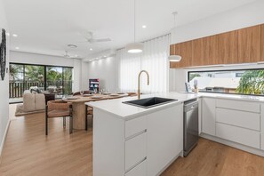 Una cocina moderna con armarios blancos, una isla central con pileta y una zona de comedor con mesa y sillas de madera.