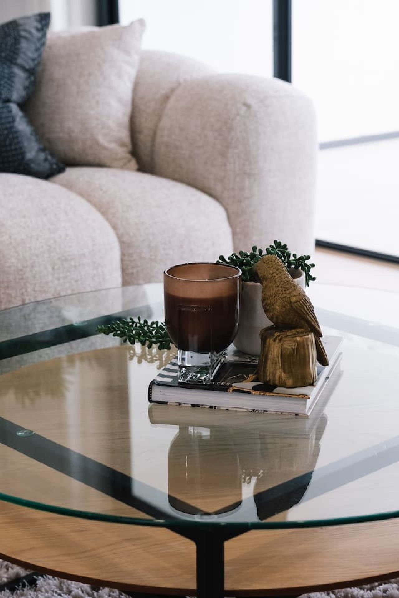 A glass coffee table with a book, a cup, and a decorative bird statue.