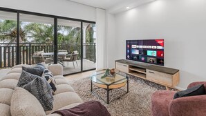 Una sala moderna con un televisor de pantalla plana grande, una mesa de centro de vidrio y un sofá con cojines estampados.