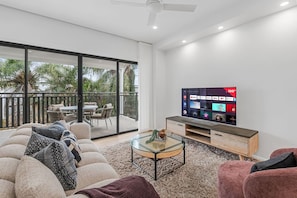 A modern living room with a large flat-screen TV, a glass coffee table, and a sofa with patterned cushions. - Brand-New Smart Home| Ducted AC | Walk to Shops (Oxley)