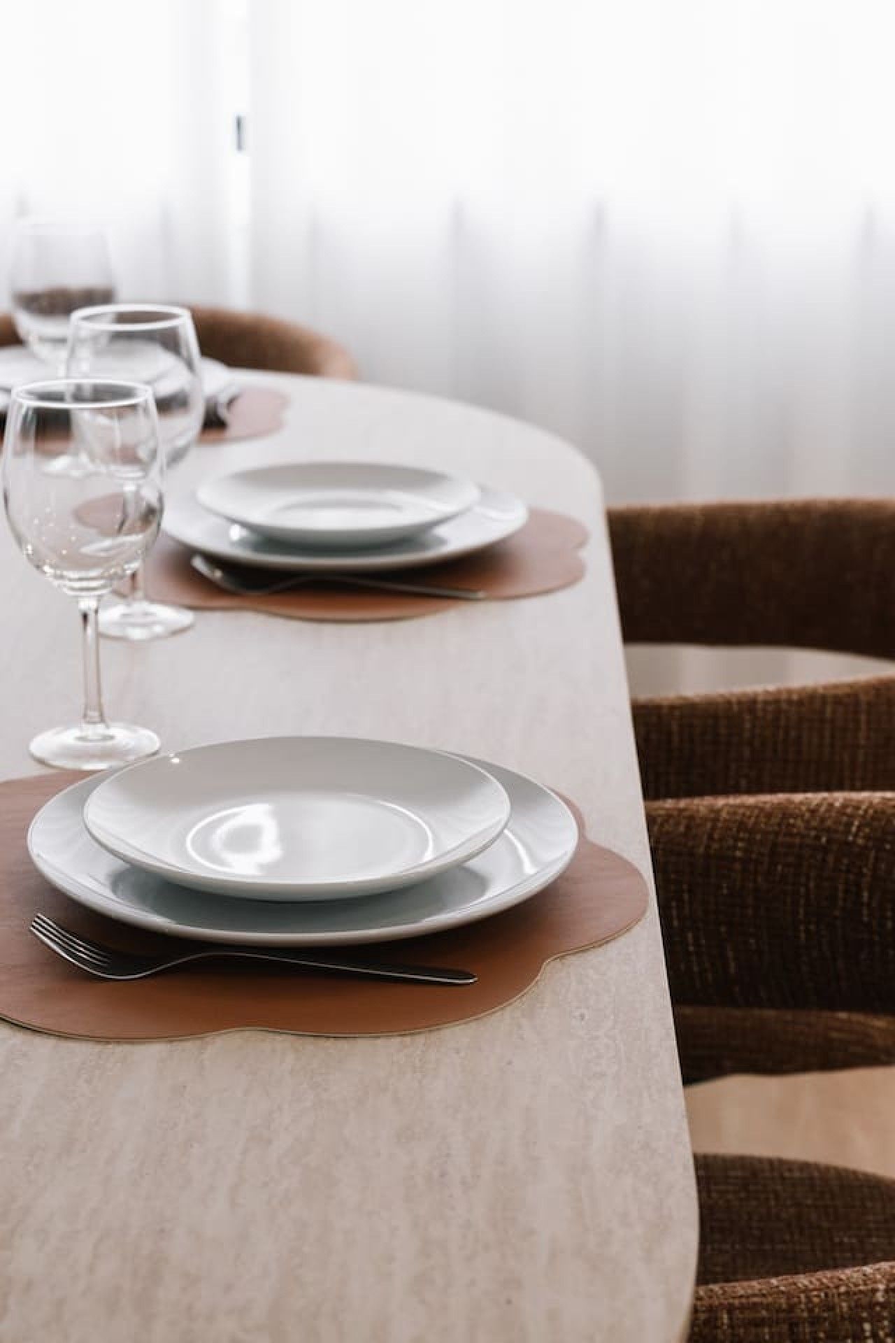 A dining table set with plates, cutlery, and wine glasses, with a chair in the background.