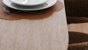 Una mesa de comedor dispuesta con platos, cubiertos y copas de vino, con una silla al fondo.