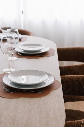 A dining table set with plates, cutlery, and wine glasses, with a chair in the background. - Brand-New Smart Home| Ducted AC | Walk to Shops (Oxley)