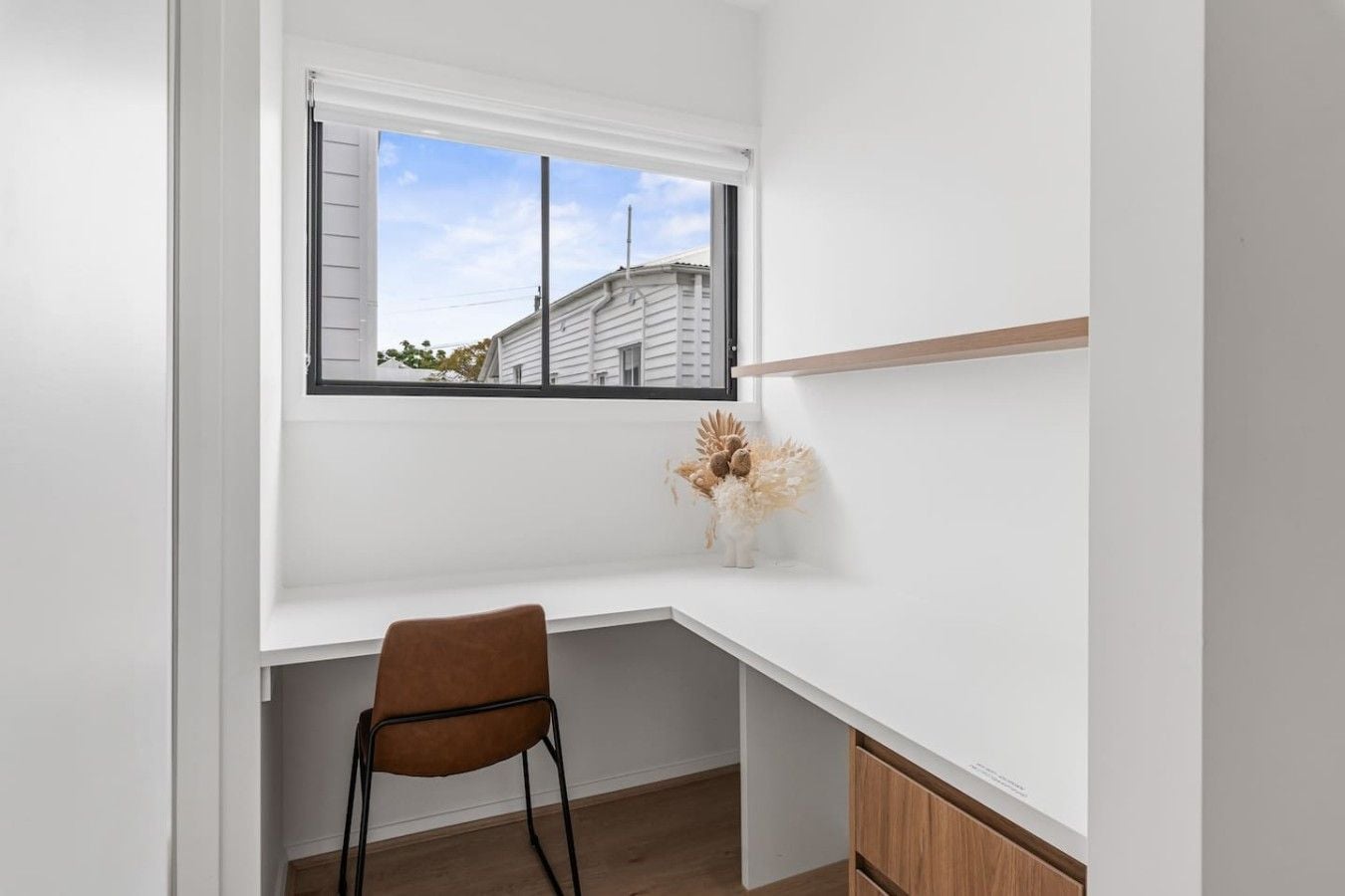 A corner desk with a chair, a window, and a small vase with dried flowers.