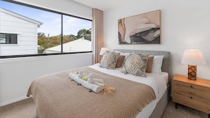 Un dormitorio con cama, mesita de noche, lámpara, ventana con vistas y un cuadro en la pared.