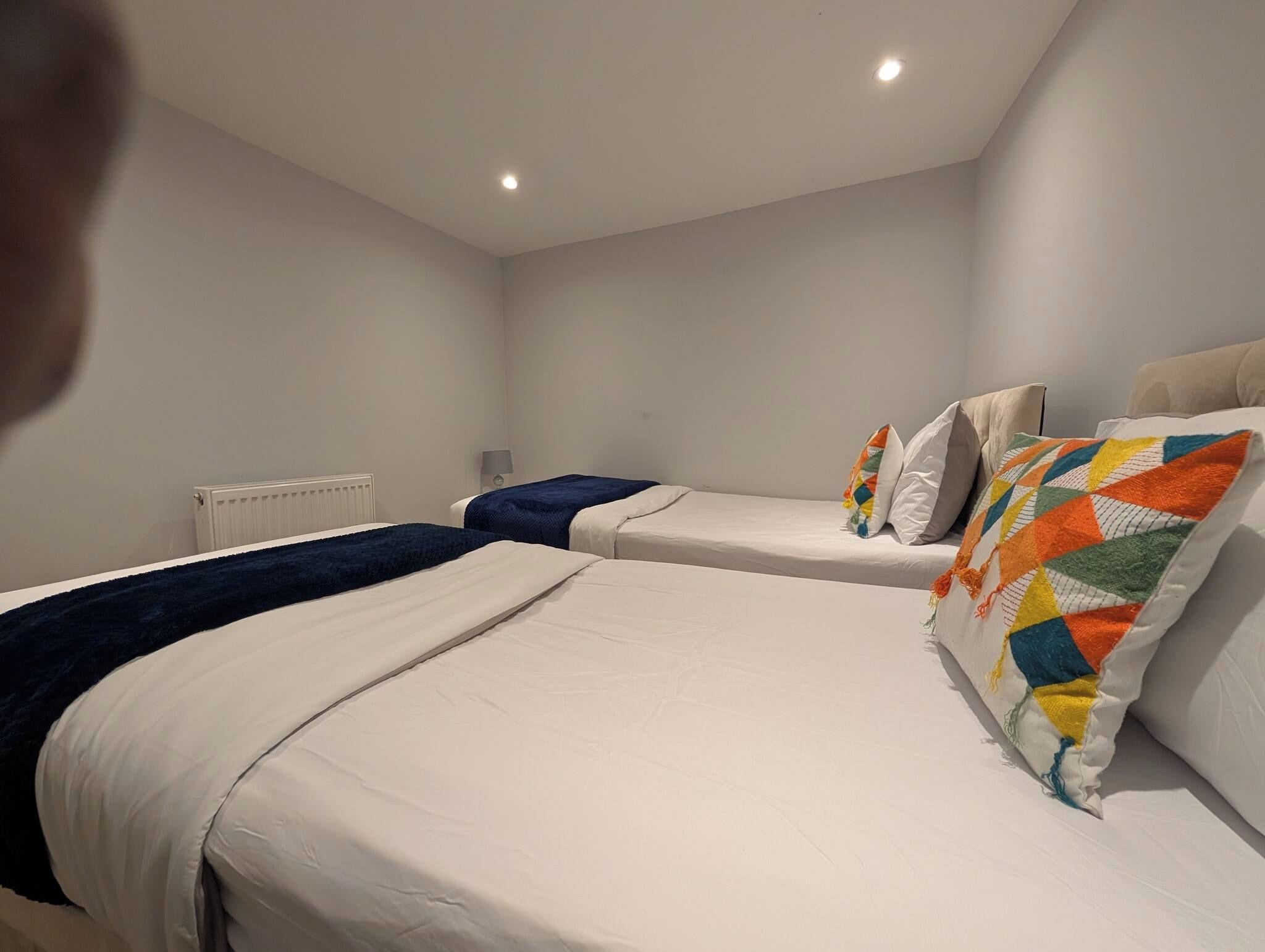 A hotel room with two beds, a radiator, and a lamp.