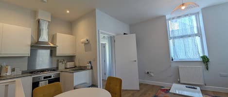 Cocina moderna con armarios blancos, estufa a gas y comedor con mesa redonda y sillas amarillas.