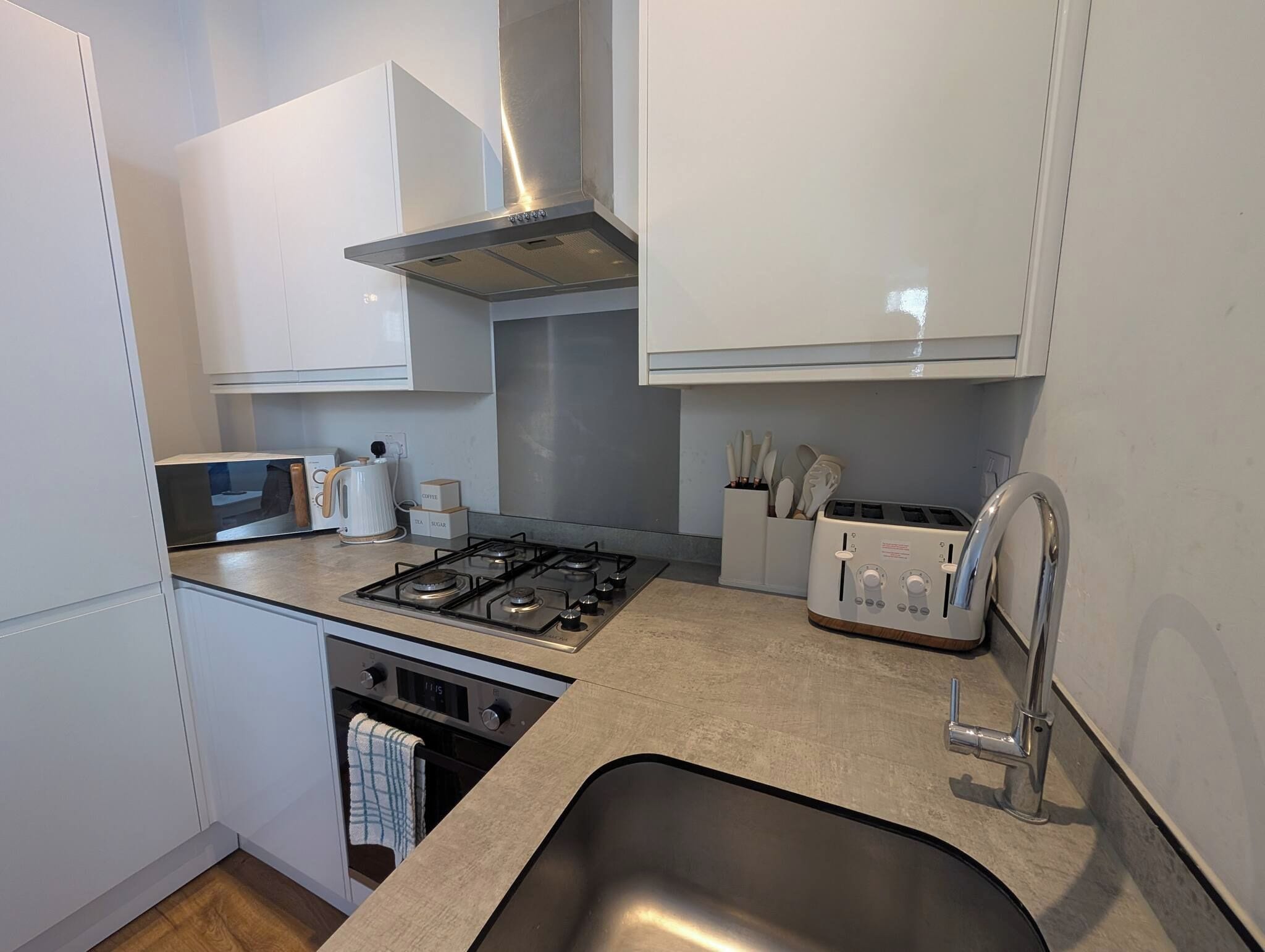 A modern kitchen with white cabinets, a gas stove, a toaster, and a stainless steel sink.