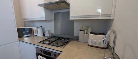 A modern kitchen with white cabinets, a gas stove, a toaster, and a stainless steel sink.