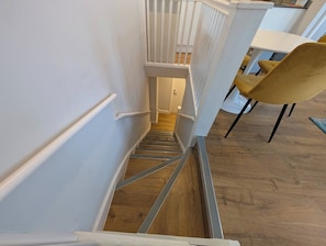 Eine Treppe mit Holzboden und weißen Wänden, die zu einem Raum mit einem weißen Tisch und einem gelben Stuhl führt.