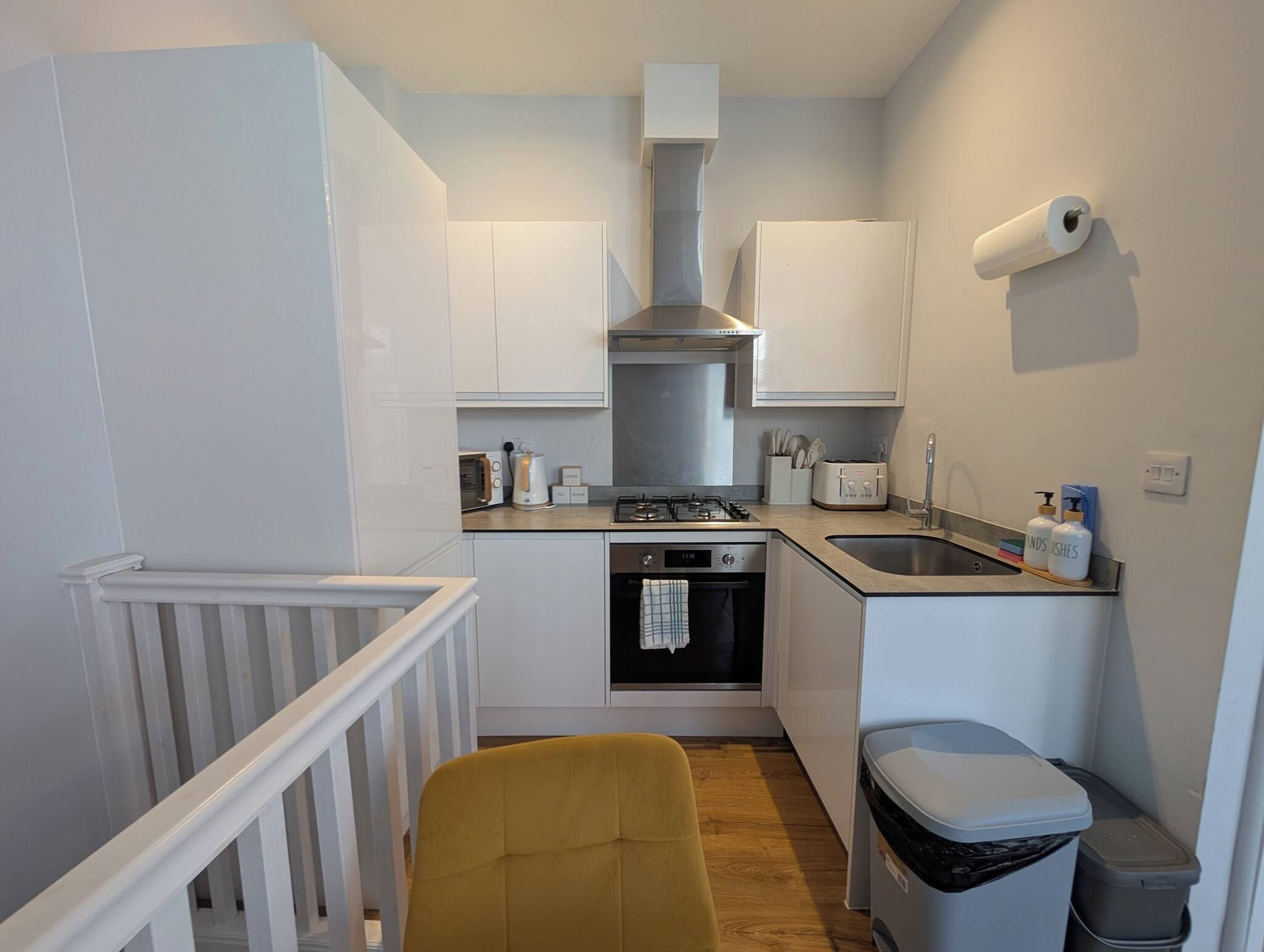 A compact kitchen with white cabinets, a gas stove, an oven, a sink, and a trash bin.