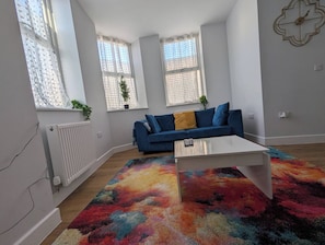 Ein modernes Wohnzimmer mit einem blauen Sofa, einem weißen Couchtisch und einem farbenfrohen Teppich.