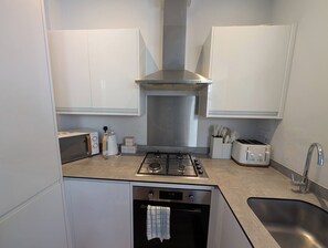 Eine kompakte Küche mit weißen Schränken, einer Edelstahl-Dunstabzugshaube, einem Gasherd, einem Toaster und einem Spülbecken.