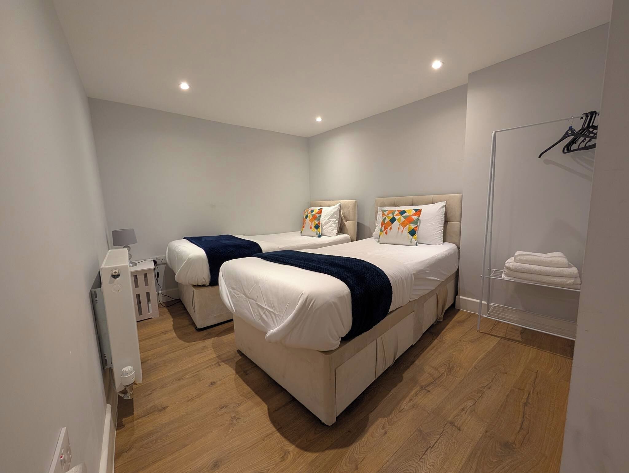 A modern bedroom with two beds, a wardrobe, and a small bedside table.