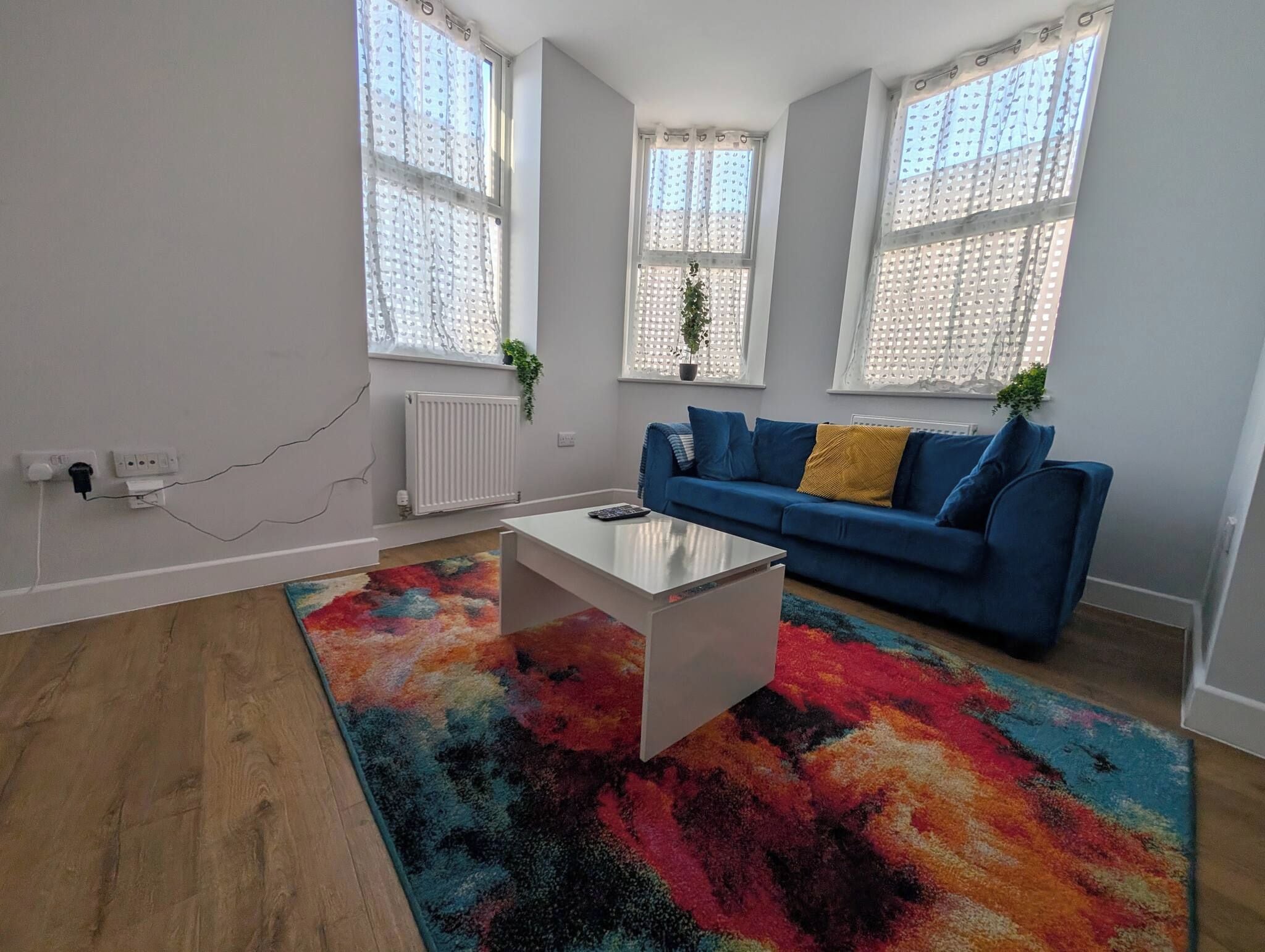A modern living room with a blue sofa, a white coffee table, and a colorful rug.
