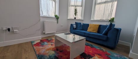 A modern living room with a blue sofa, a white coffee table, and a colorful rug.