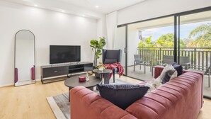 Una sala de estar moderna con un televisor de pantalla plana grande, un sofá, una mesa de centro y un balcón con mobiliario exterior.
