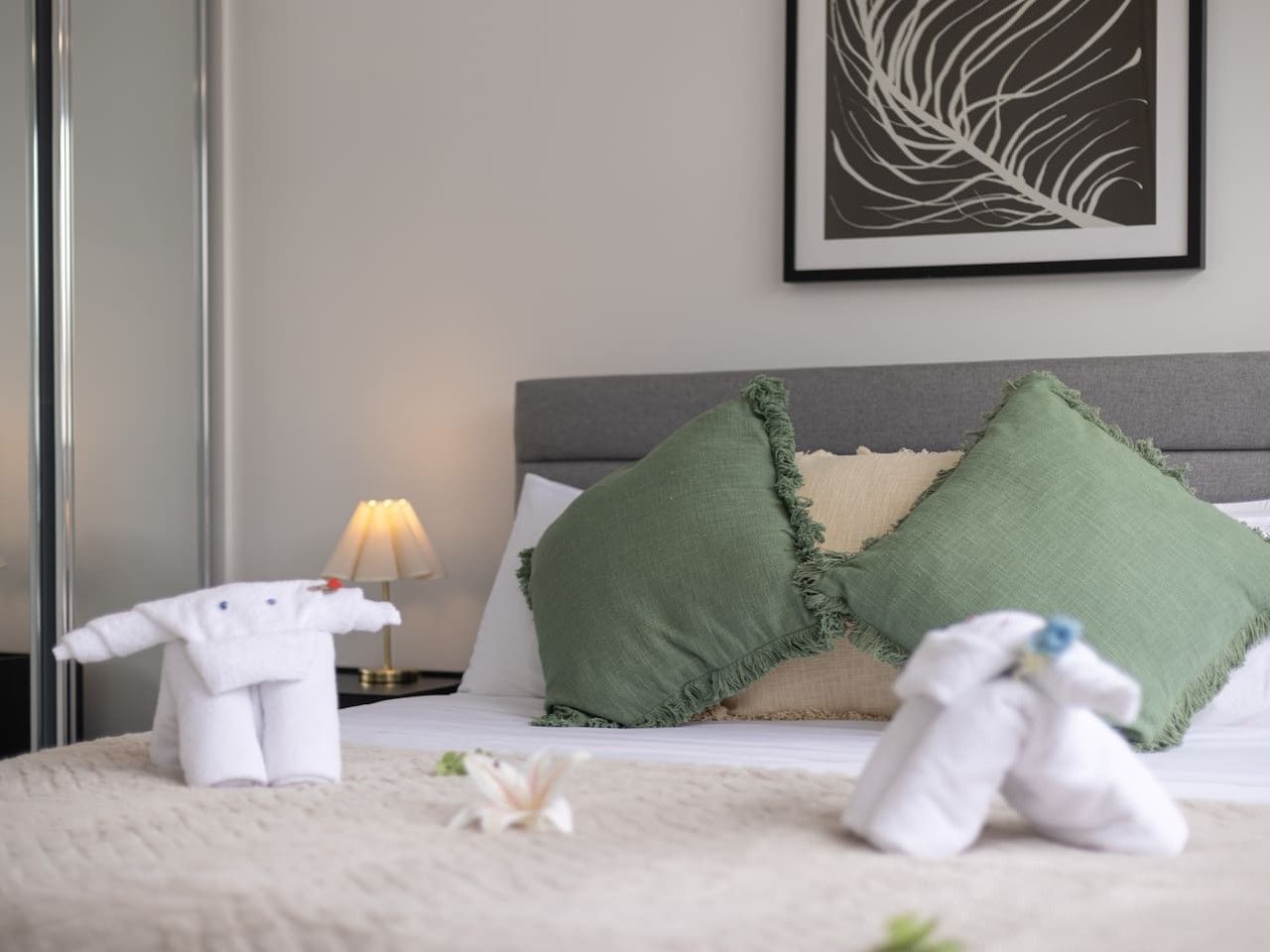 A neatly made bed with two pillows, a bedside lamp, and a framed artwork on the wall.