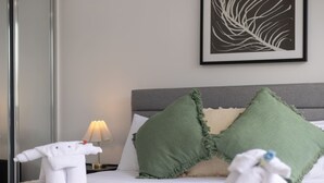 Una cama bien tendida con dos almohadas, una lámpara de noche y un cuadro en la pared.