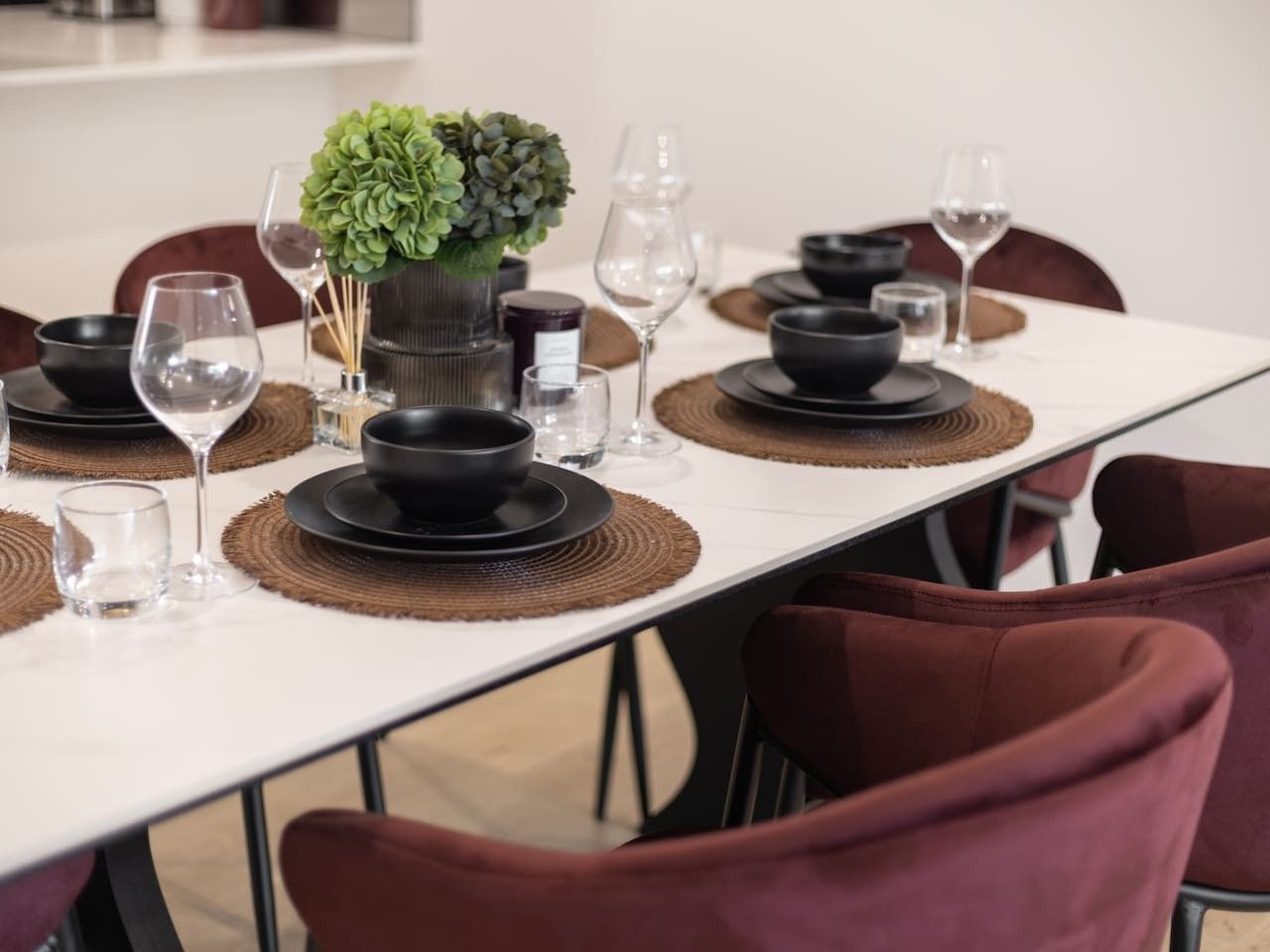 A dining table set with black plates, bowls, and glasses, accompanied by a green plant centerpiece.