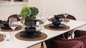 Una mesa de comedor dispuesta con platos, tazones y vasos negros, acompañada por un centro de mesa con una planta verde.