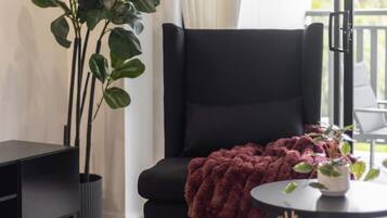 A modern living room with a black armchair, a round table with a red blanket, and a potted plant.