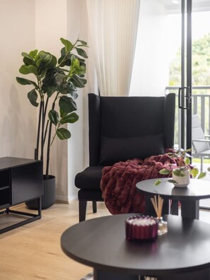 A modern living room with a black armchair, a round table with a red blanket, and a potted plant. - Brand-New Smart Home |3 Min Walk to Train & Shops (Oxley)