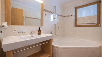 Une salle de bain avec un lavabo blanc, un miroir, une douche et une fenêtre.
