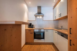 A compact kitchen with wooden cabinets, a stainless steel oven, and a built-in range hood. - Alpenchalet Vital (Neustift im Stubaital)
