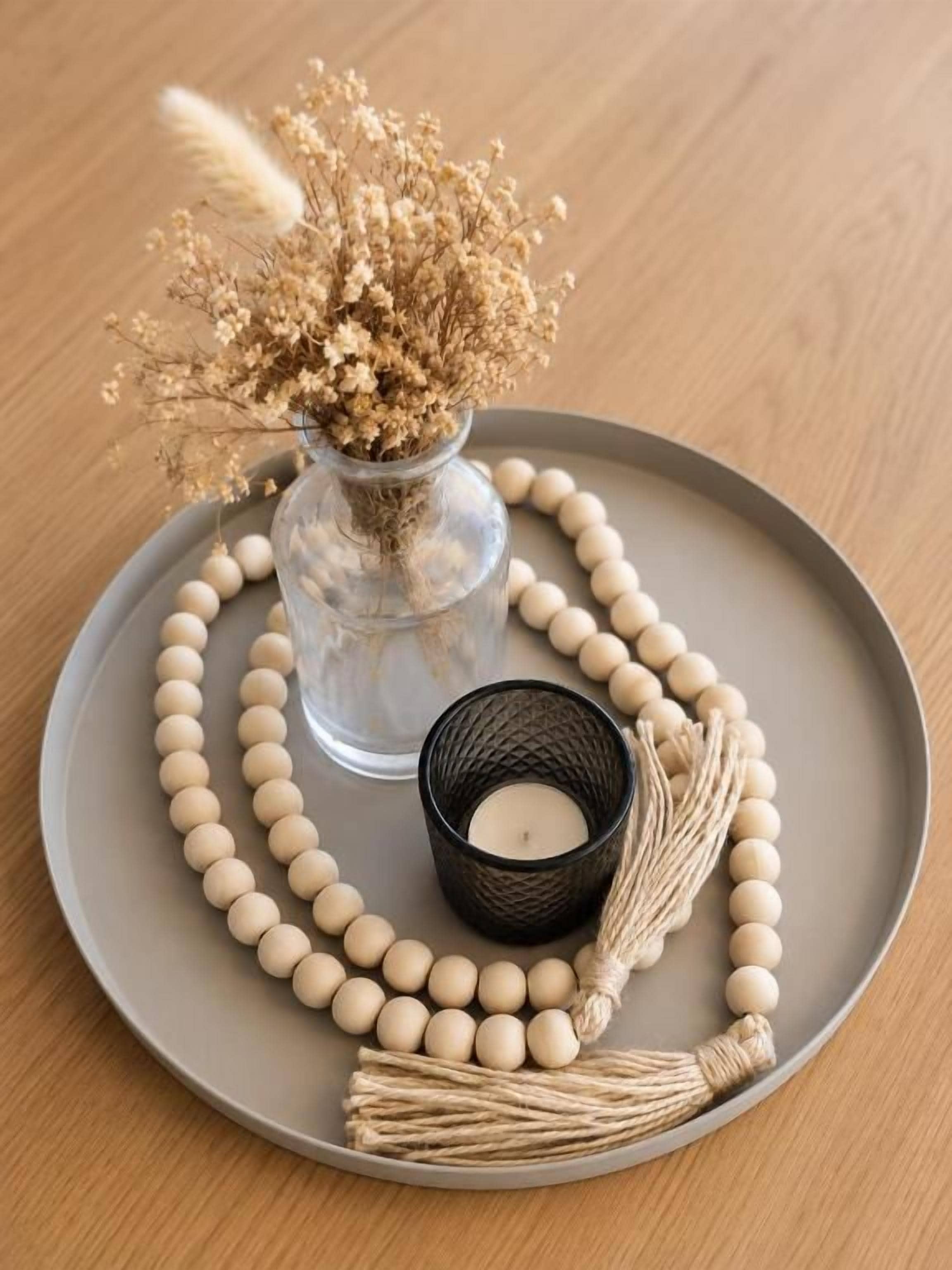 Un plateau sur lequel se trouvent un vase en verre contenant des fleurs séchées, une bougie dans un porte-bougie noir et un collier orné de perles.